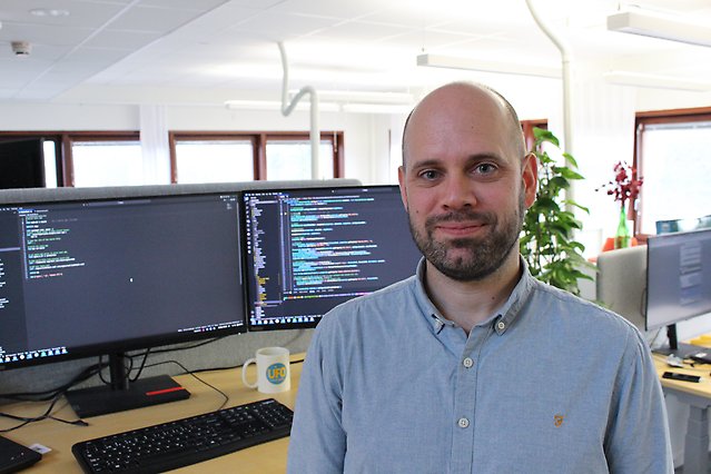 Jonas, systemutvecklare i ljust kontorslandskap med bildskärmar och växter i bakgrunden.