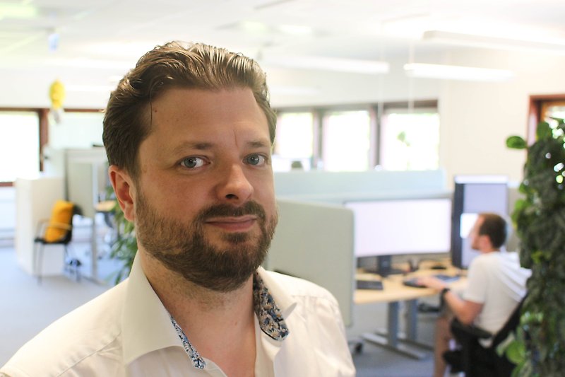 Eric, medelålders man med skägg i ett ljust kontorslandskap med gröna växter.