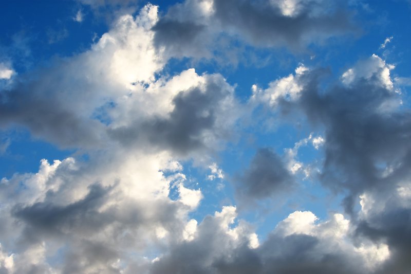 Mörka och ljusa, solbelysta moln sedda underifrån mot en blå himmel. 