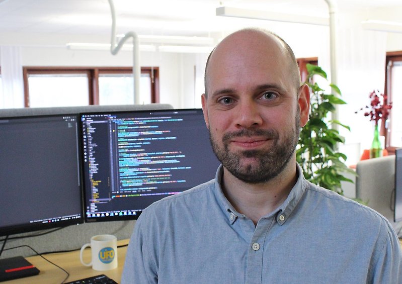 Jonas, systemutvecklare i ljust kontorslandskap med bildskärmar och växter i bakgrunden.