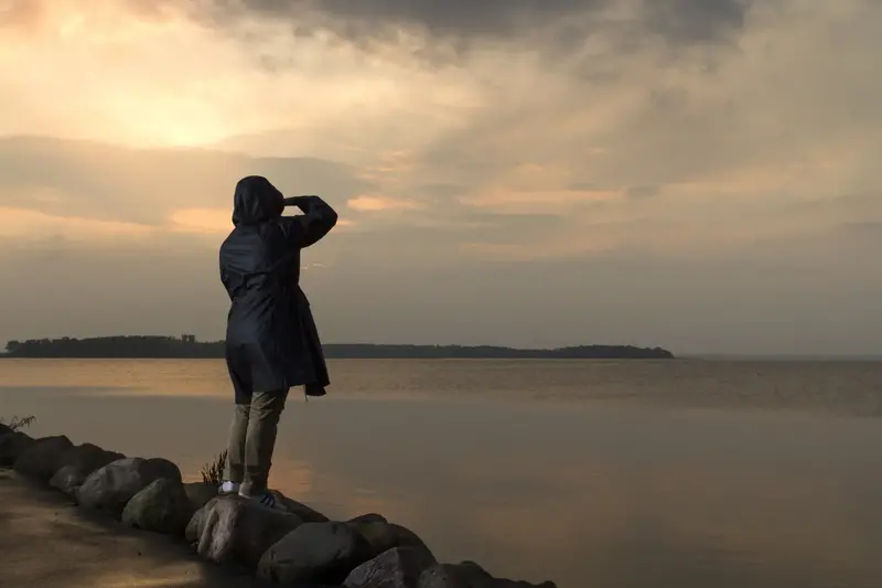 Kvinna står och tittar ut på en solnedgång från en hamn