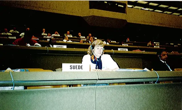 Gunlög med headset som svensk delegat i en stor konferenssal.