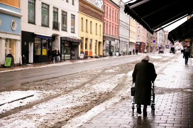 Bild på äldre sam som går längs trottoar med slask runt om