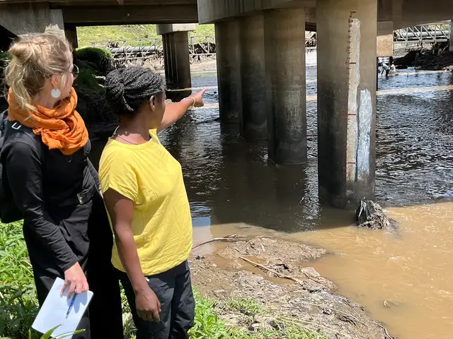Två personer vid en flod varav den ena pekar på en handmålad vattennivåmätare på ett brofundament.
